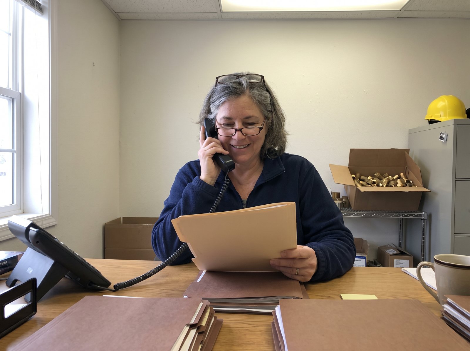 Contractor office manager on the phone following up on an unpaid invoice with job folders on her desk