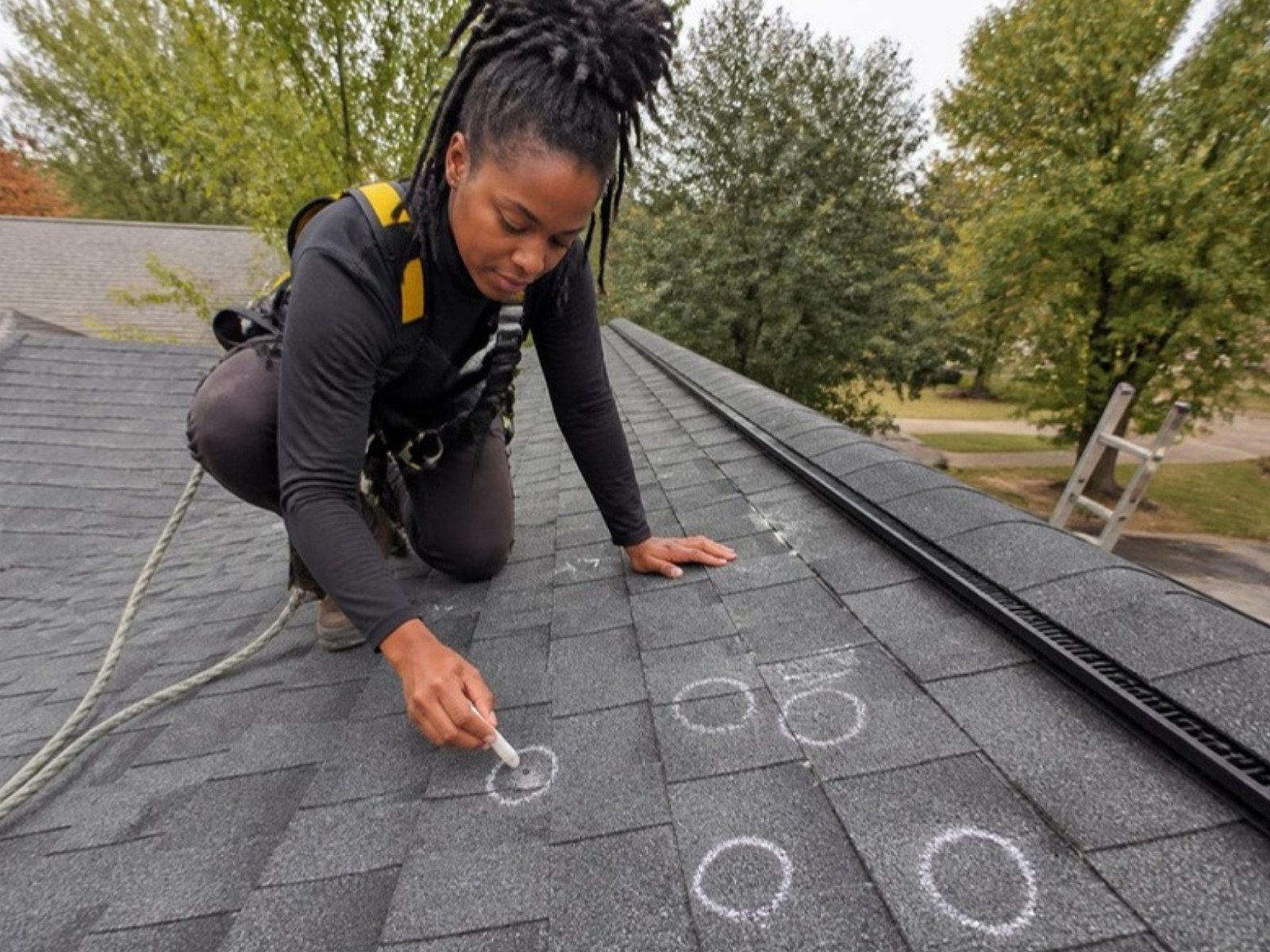 Roofing inspector circling hail hits on asphalt shingles with chalk during a storm inspection