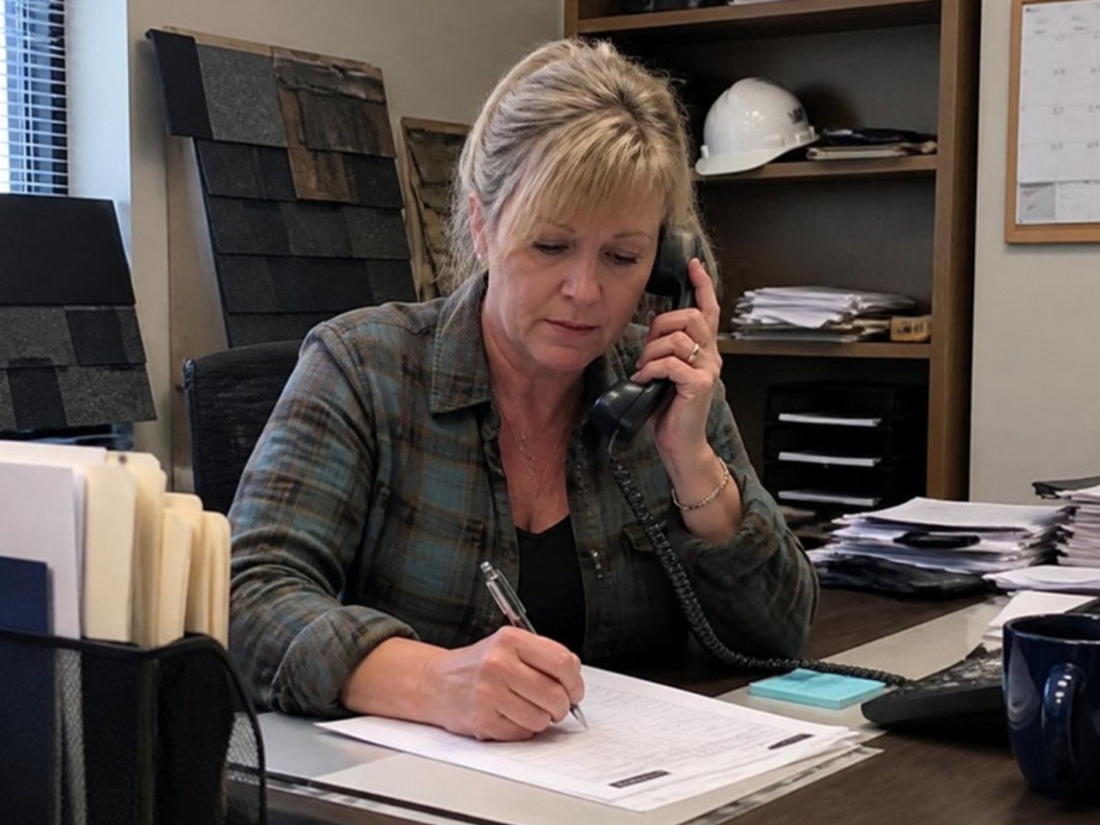 Roofing office manager on the phone logging a new lead on a paper lead sheet