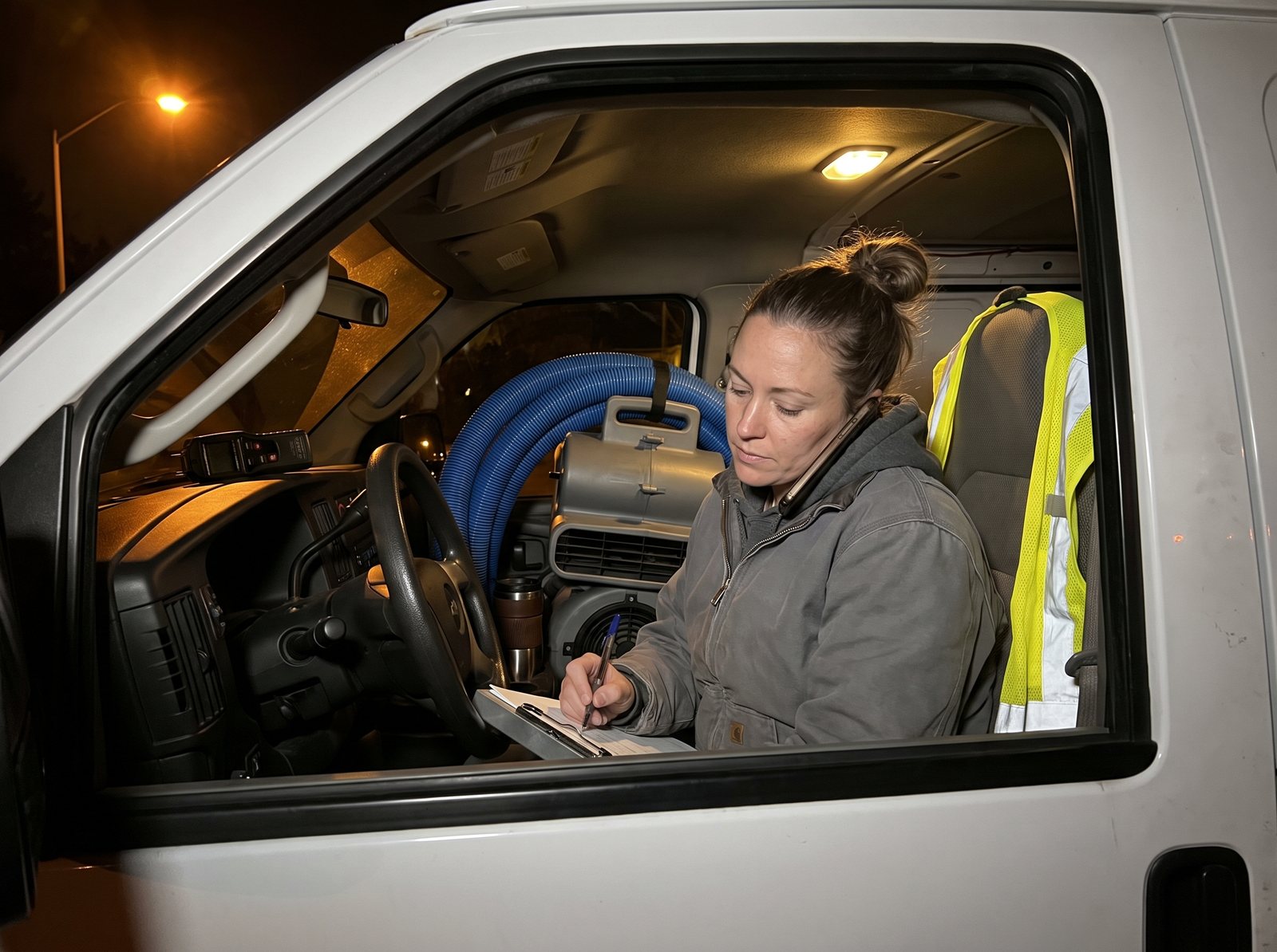 On-call restoration crew lead taking an emergency water damage call from her van at night